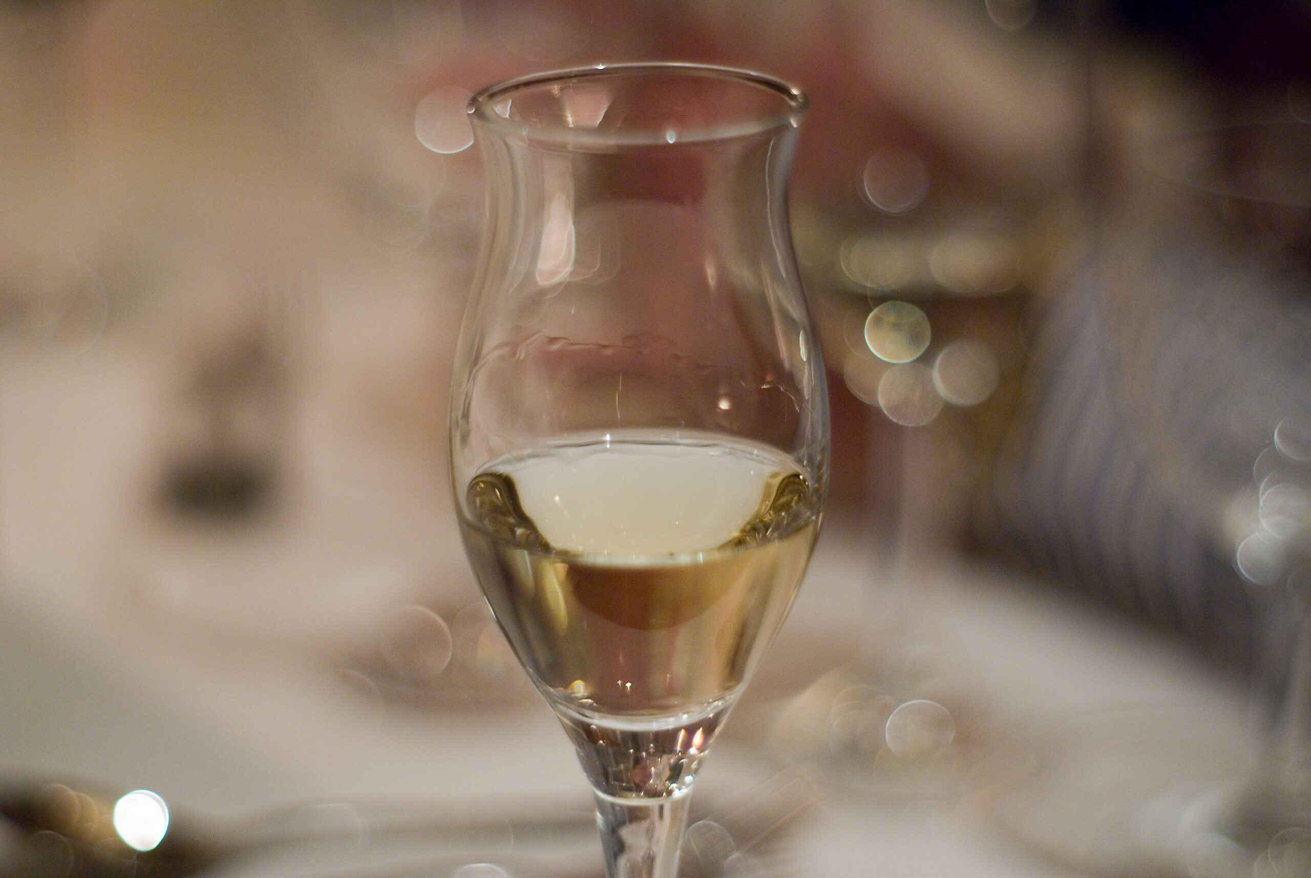 Piccolo calice a tulipano con distillato trasparente accanto a una bottiglia su un tavolo di legno