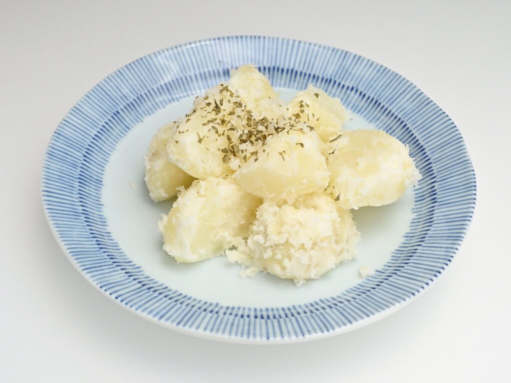 Patate lessate e pelate ancora calde su un vassoio, accanto a uno schiacciapatate