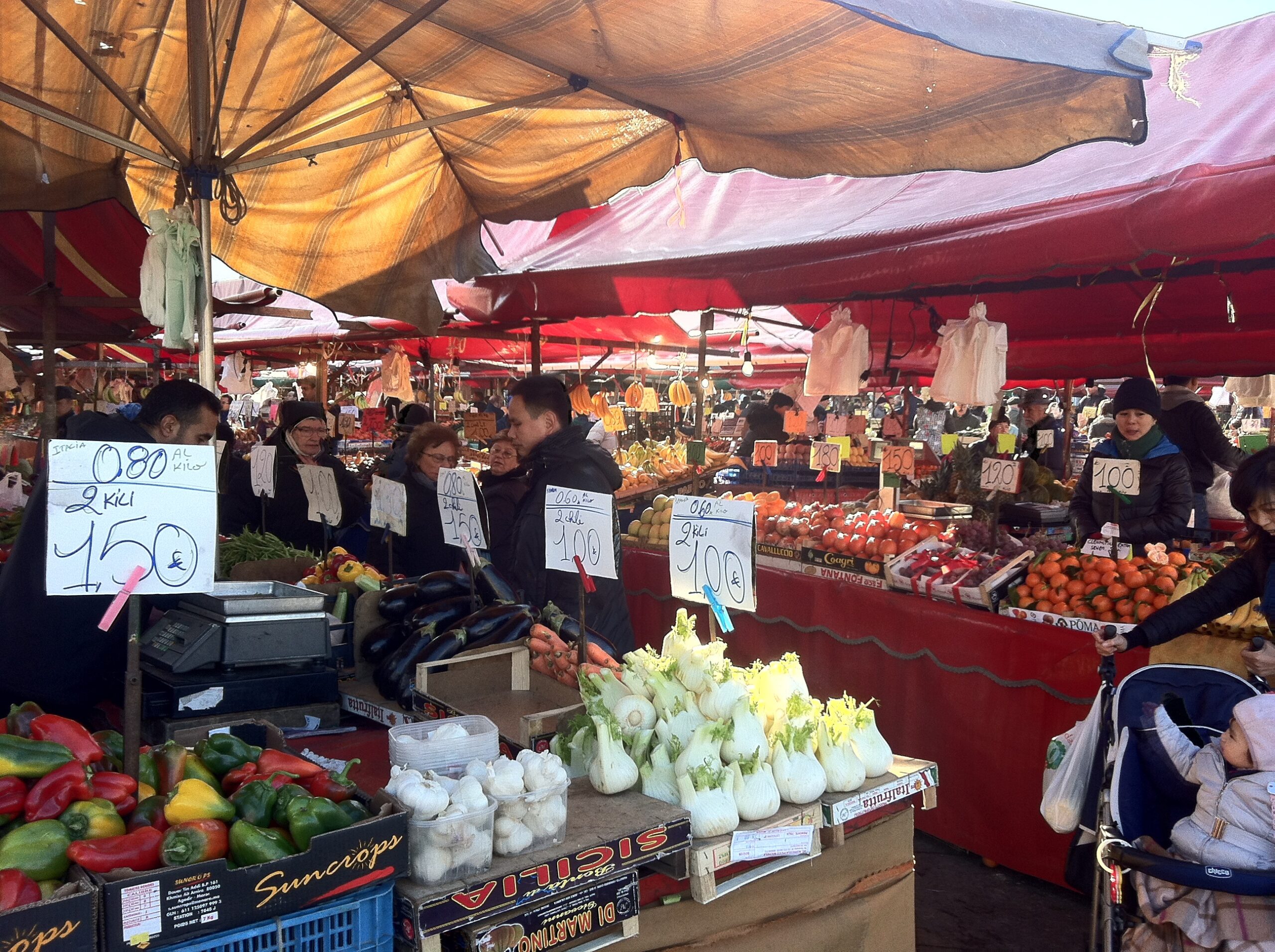 Banchi affollati di un grande mercato all'aperto con tettoie e cassette di frutta esposte