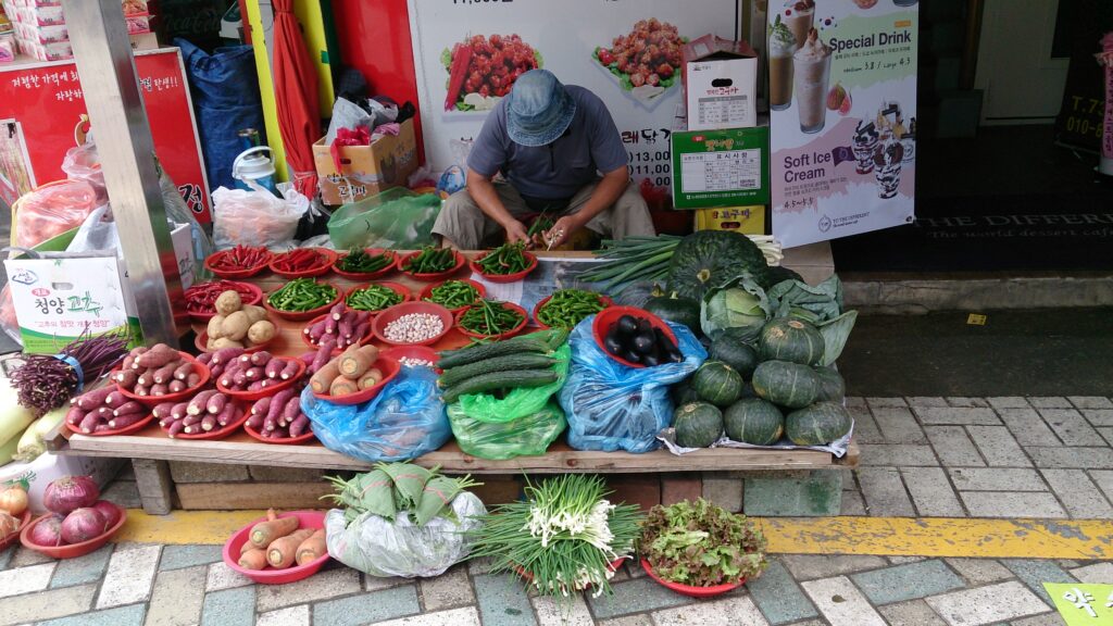 Banco di verdure con cassette di peperoni, zucchine e insalate e cartellini dei prezzi