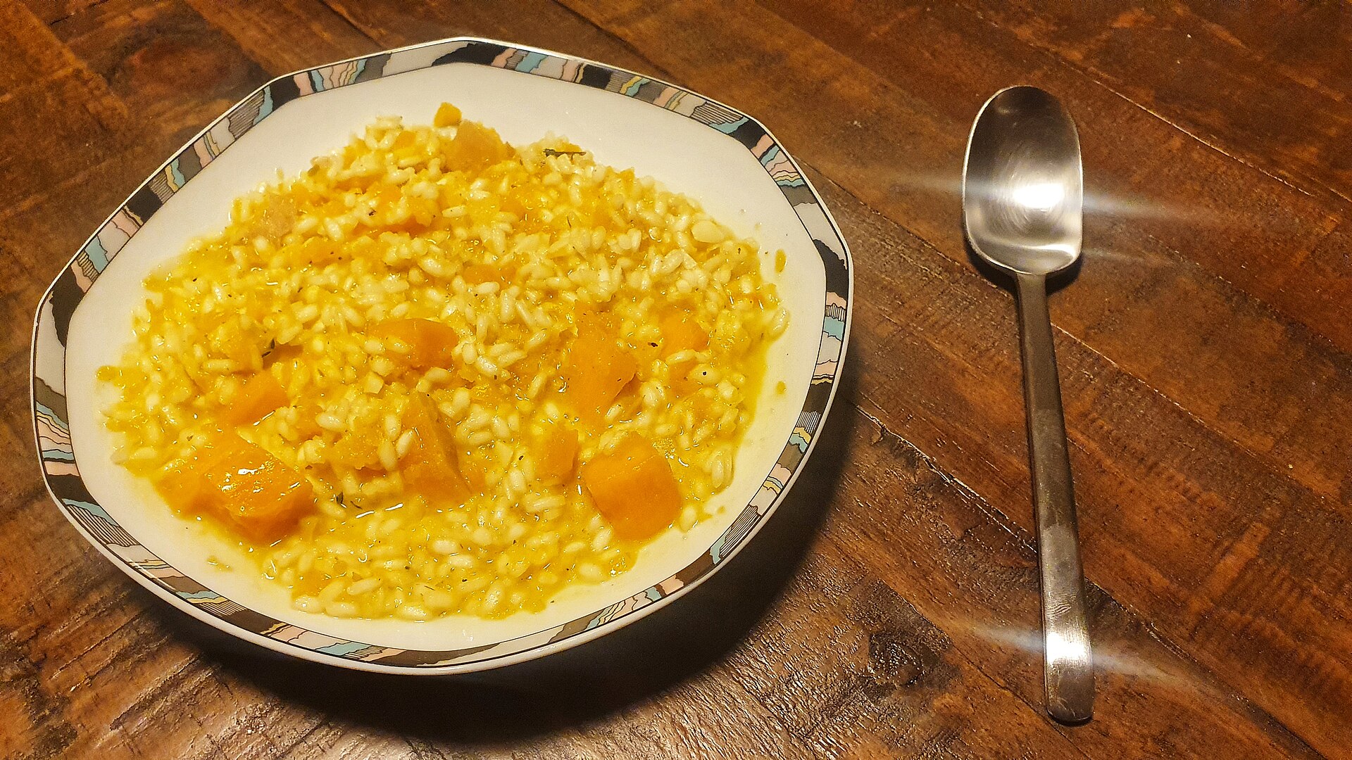 Piatto fondo con risotto arancione mantecato e briciole chiare sparse sulla superficie